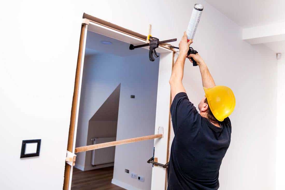 Construction-worker-installing-door-in-home.-Handyman-installing-door-with-an-mounting-foam-in-a-room.-Worker-assembles-the-door-frame